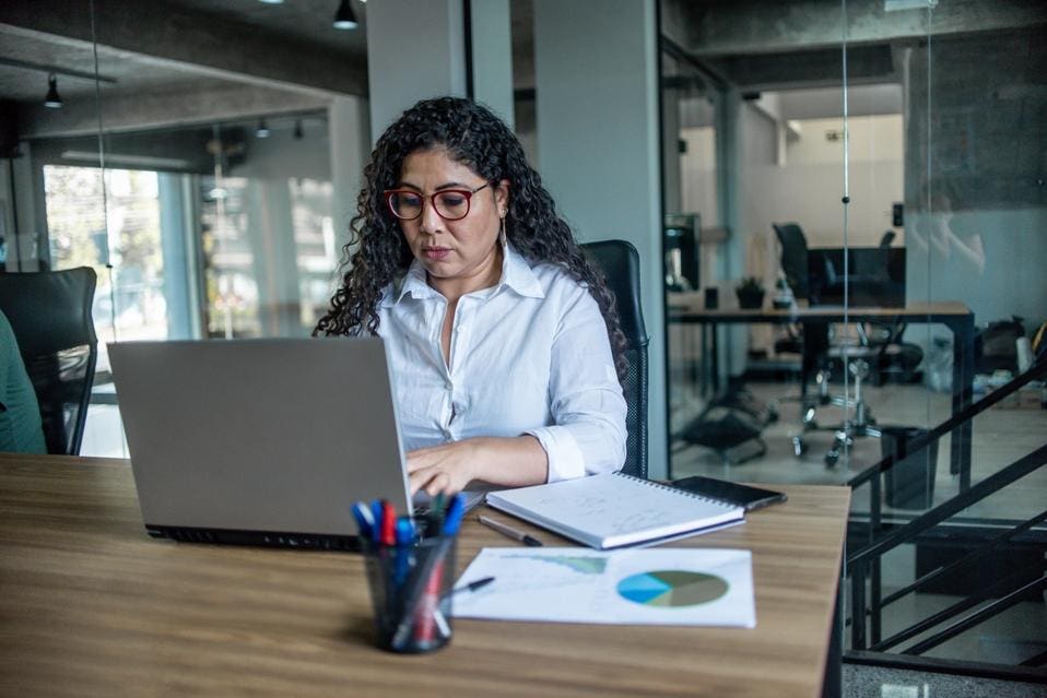 https://imageio.forbes.com/specials-images/imageserve/645c50eaf8457defdf9c026c/Latin-woman-working-in-a-coworking-space--Woman-sits-at-a-table-with-computer-before/960x0.jpg?format=jpg&width=1440